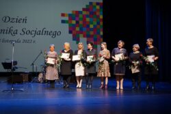 Osiem kobiet stojących na scenie. Każda z kobiet trzyma w rękach kwiat i dyplom.