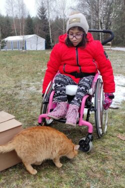 Dziewczynka na wózku inwalidzkim i stojący przed nią kot.
