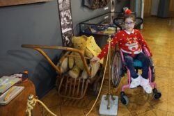 Dziewczynka na wózku inwalidzkim stojąca obok wózka z misiem.