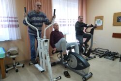 Trzech mężczyzn ćwiczących na urządzeniach rehabilitacyjnych. 