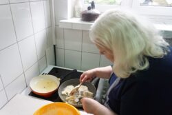 Kobieta stojąca przy kuchence na której stoi patelnia i inne naczynia.