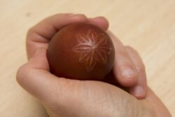 Jajko z wydrapanym wzorem trzymane w dłoni.