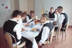 Grupa osób siedząca przy stole na którym stoją talerze z jedzeniem.