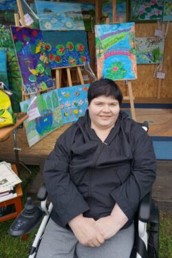 Kobieta na wózku inwalidzkim przed wystawą obrazów.