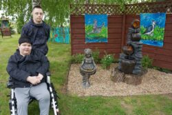 Kobieta na wózku inwalidzkim i stojący za nią chłopiec obok zaaranżowanego miejsca w ogrodzie.