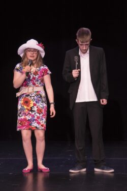 Dziewczyna i chłopak z mikrofonami w ręku stojący na scenie.