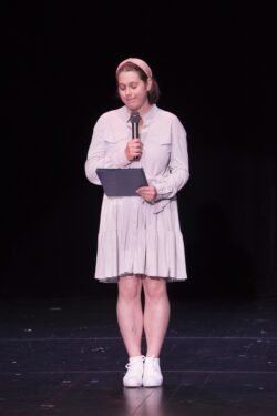 Dziewczyna z mikrofonem w ręku stojąca na scenie.