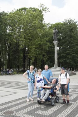 Zdjęcie grupowe. Pięć osób stojąca na placu przed kolumną z rzeźbą.