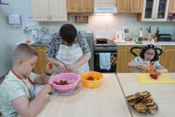Chłopiec i dwie dziewczynki przy dużym stole kuchennym obierają i kroją truskawki.