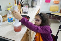 Dziewczynka przy blacie kuchennym miksująca truskawki w naczyniu.