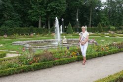 Kobieta stojąca w parku na tle kolorowych kwiatów i fontanny.