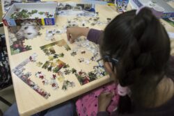 Siedząca przy stole dziewczynka układająca puzzle.