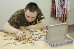 Siedzący przy stole chłopiec układający puzzle.