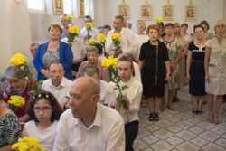 Grupa osób z kwiatami siedząca i stojąca w kaplicy.