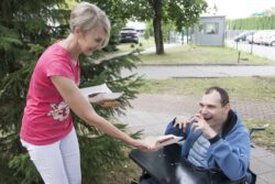 Kobieta podaje kiełbaskę na talerzyku chłopcu na wózku inwalidzkim.