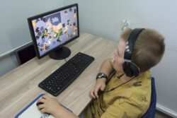 Chłopiec ze słuchawkami na uszach siedzący przed monitorem komputera.
