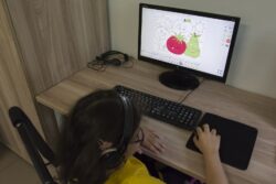 Dziewczynka ze słuchawkami na głowie siedząca przed monitorem komputera.