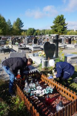 Dwie osoby porządkujące groby na cmentarzu.