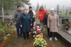 Grupa osób stojąca przy grobie na cmentarzu.