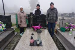 Trzy osoby stojące przy grobie na cmentarzu.