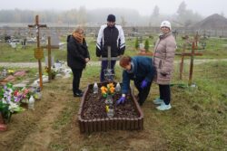 Grupa osób porządkująca grób na cmentarzu.