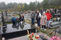 Grupa osób stojąca przy grobie na cmentarzu.