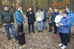 Grupa osób stojąca na alejce w lesie. Jeden z mężczyzn trzyma w ręku mikrofon.