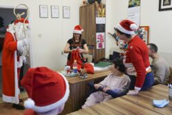 Mikołaj wchodzący do pomieszczenia w którym przy stolikach siedzą osoby w różnym wieku.