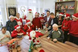 Zdjęcie dużej grupy osób w różnym wieku z Mikołajem siedzących i stojących za dużym stołem.