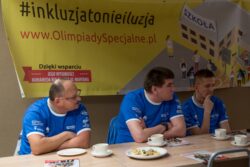 Trzech mężczyzn siedzących przy stole. Za nimi wisi baner z napisem #inkluzjatonieiluzja www.Olimpiady Specjalne.