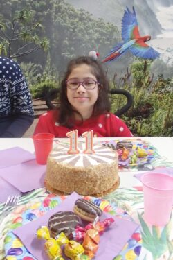 Siedząca przy stole dziewczynka przed którą stoi tort.