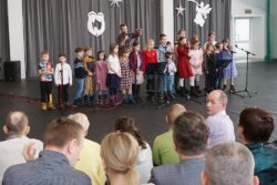 Duża grupa dzieci stojąca przed mikrofonami na dużej sali na przeciw siedzących osób.