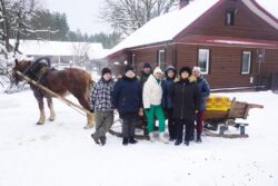 Grupa ciepło ubranych osób stojąca przed saniami zaprzężonymi w konia.