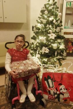 Dziewczynka na wózku inwalidzkim z prezentami przy choince.