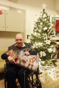 Mężczyzna na wózku inwalidzkim z prezentem przy choince.