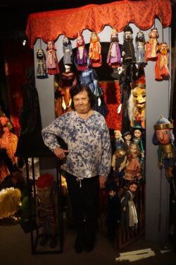 Kobieta stojąca w pomieszczeniu z różnymi lalkami teatralnymi.