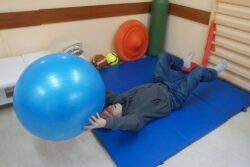 Mężczyzna wykonujący ćwiczenia z dużą piłką na materacu w pozycji leżącej na plecach.