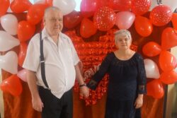 Trzymający się za ręce mężczyzna i kobieta na tle czerwonej dekoracji.