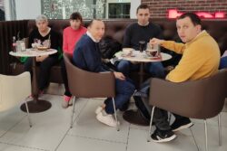 Grupa osób siedząca w kawiarni przy stolikach.