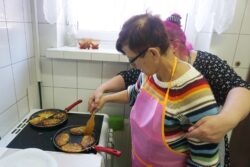 Stojąca przy kuchence dwie kobiety smażące placki ziemniaczane.