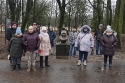 Grupa osób stojąca w parku przy rzeźbie psa Kawelina