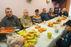 Grupa osób siedząca przy stole na którym leżą różne owoce.