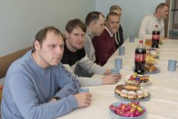 Grupa siedzących przy stole mężczyzn na którą stoją talerze ze słodyczami i butelki z napojami.